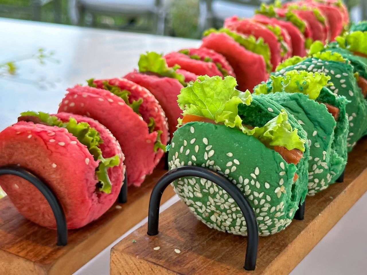 Mini-burgers coloridos rosa e verde com gergelim em suporte de madeira