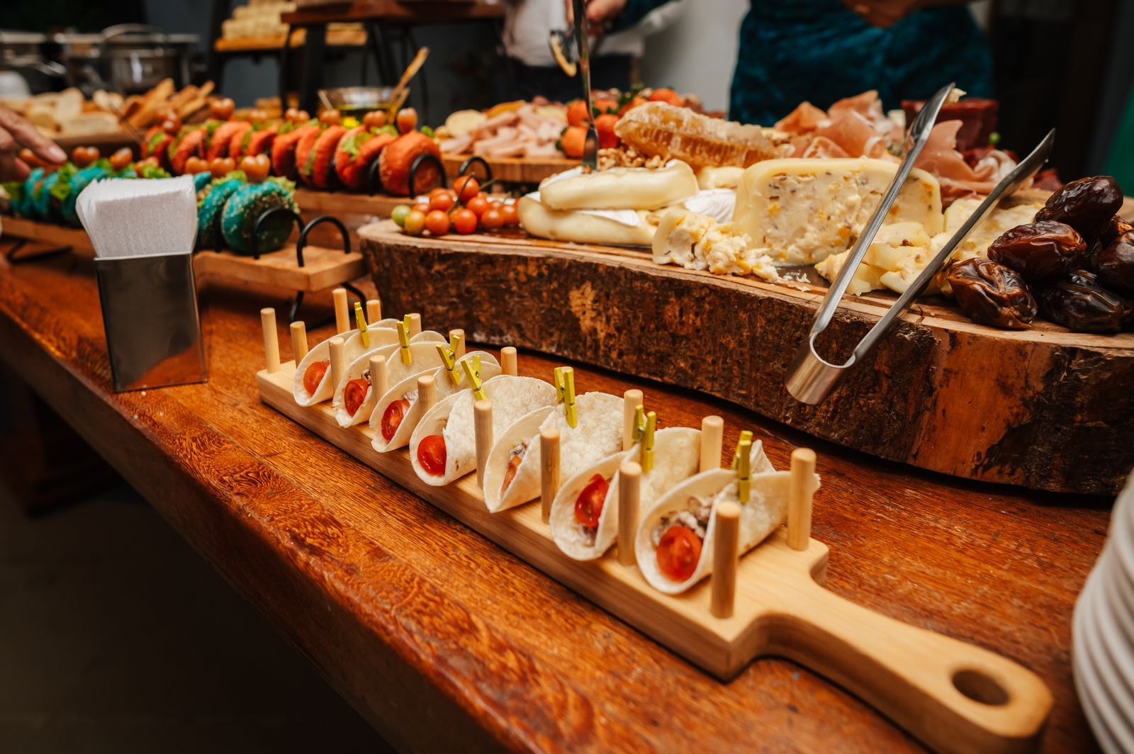 Mesa de buffet com mini-tacos em suporte de madeira, tábua de frios e queijos variados