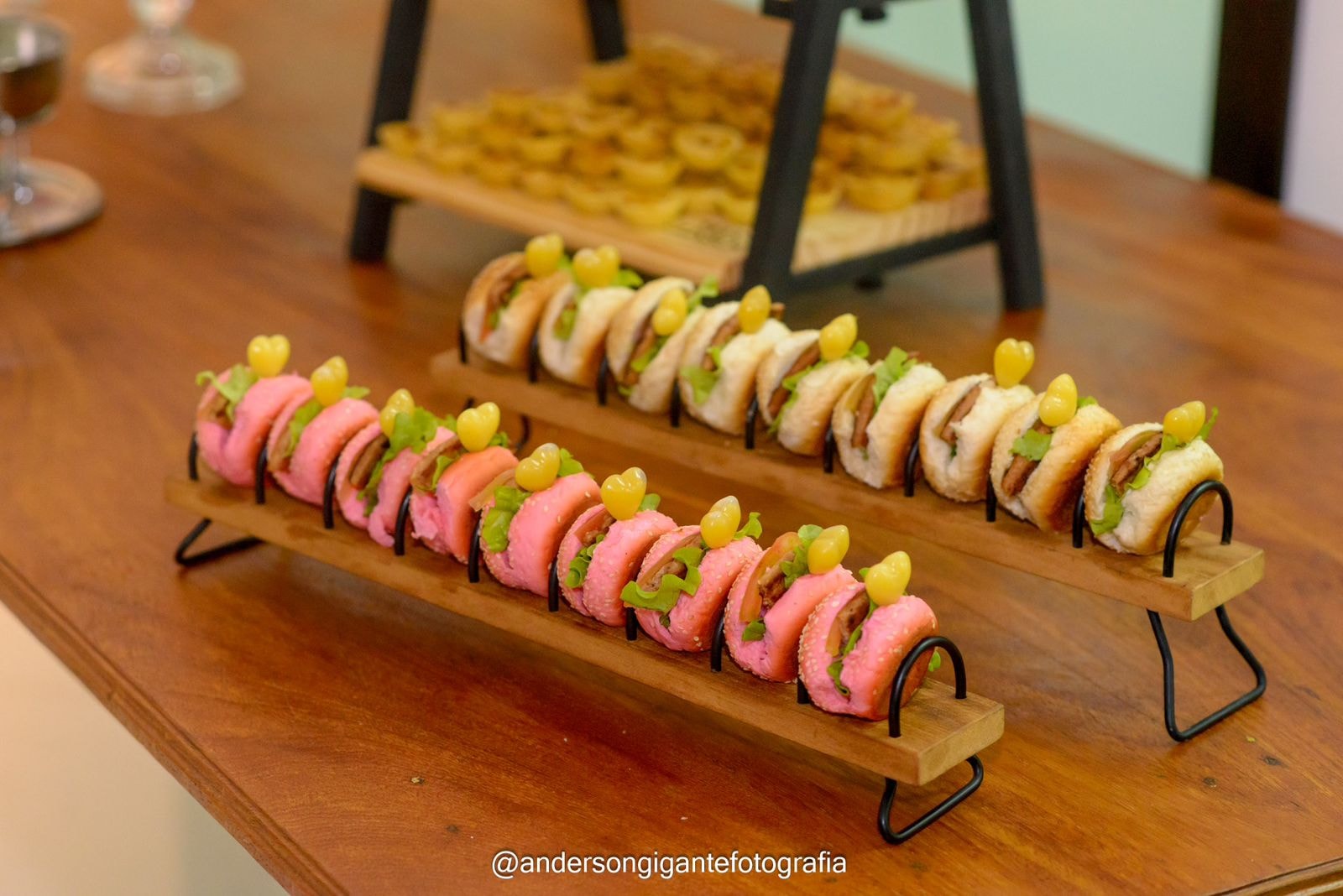 Mini-burgers rosa e branco em suporte de madeira com prendedores dourados