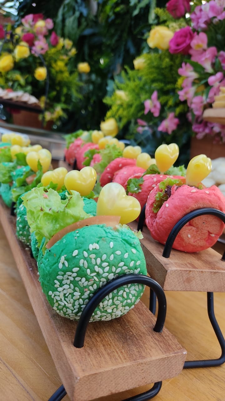 Mini-burgers coloridos verde e rosa com gergelim e palito coração em suporte de madeira